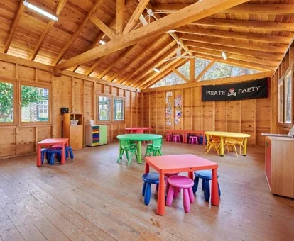 Vista del club infantil con actividades con suelo de parque y techos de madera y con unas mesas para las actividades de los más pequeños.