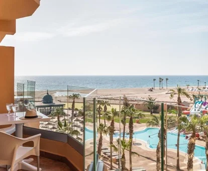 Mesa con unas sillas y una copa con vistas a la playa y la piscina con toboganes