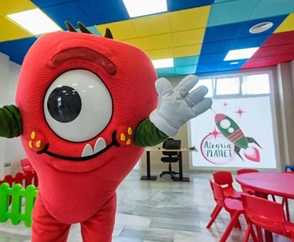 Zona del club infantil con unas mesas para hacer actividades infantiles y la mascota del hotel en un lado