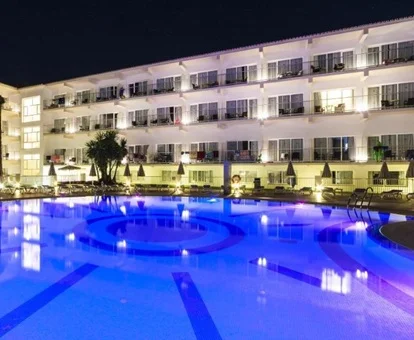 Piscina por la noche iluminada donde se puede ver las mesas del bar y las habitaciones del fondo