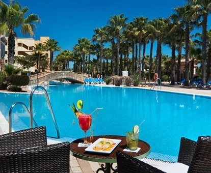 Terraza del bar que se encuentra junto a la piscina con una mesa con un par de preparados y dos sillas