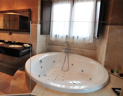 Foto del jacuzzi circular para parejas que se encuentra en la habitación suite en el baño acristalado que se puede ver desde la cama.