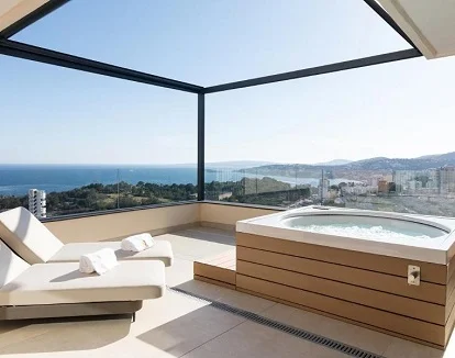 Foto de la Suite Shapire The Royal solo para adultos donde tienes unas tumbonas y un jacuzzi con vistas al mar y la montaña a través de una terraza acristalada.