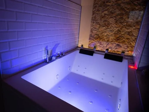Foto del jacuzzi con cromoterapia y chorros de hidromasaje con una cristalera en los lados que lo separan de la cama en el dormitorio del apartamento Vistas Chamberi