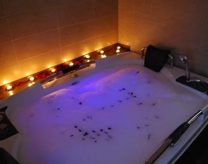 Foto del jacuzzi para dos personas con velas en los bordes y luz azul de cromoterapia