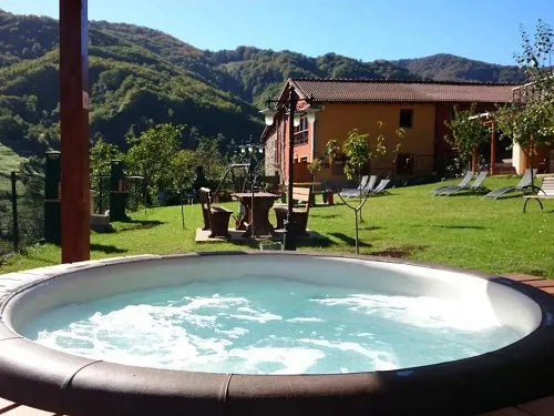 Jacuzzi exterior bajo un techado en medio de la naturaleza rodeado de cesped
