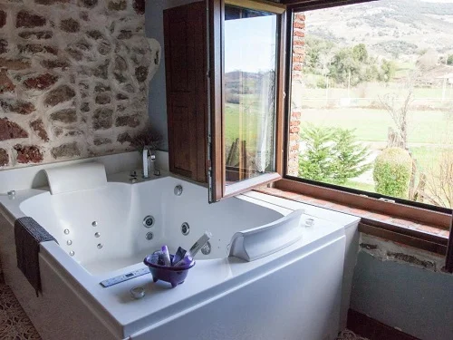 Jacuzzi para parejas junto a la ventana en la Suite Clásica con decoración rústica y vigas de madera en la casa rural Posada La Corralada