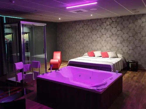 Jacuzzi rectangulara para parejas bajo una luz morada junto a la cama y al lado de la ducha en la Suite Junior.