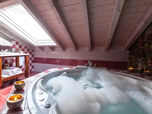 Jacuzzi lleno de espuma y con velas en el borde bajo el techo abuhardillado madera en la Suite Junior con jacuzzi en el hotel rural Casona La Hondonada