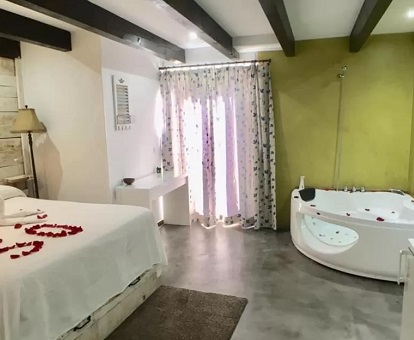 Foto de la cama con pétalos de rosa y el jacuzzi de tipo circular que se encuentra enfrente en la habitación Triple Deluxe del Albergue Boi Romanic Suites.