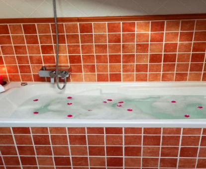 Foto de la bañera de hidromasaje con espuma y pétalos de roda de la casa rural Can Castell de Rocabruna