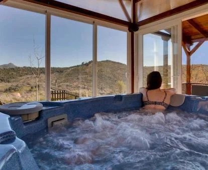 Foto del jacuzzi de gran tamaño con los chorros de hidromasaje funcionando y con una chica en el borde del jacuzzi disfrutando de las vistas al campo y la sierra.