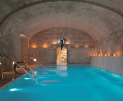 Piscina interior estilo rustica, que cuenta con fuentes, duchas y sistema de hidromasaje del Spa ubicado en el hotel Jardí de Ses Bruixes en Mahón