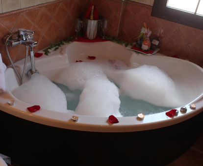 Foto de la bañera de hidromasaje con espuma y pétalos de rosa que se encuentra en ele Hotel Rural Valle del Turrilla - Cazorlatur

