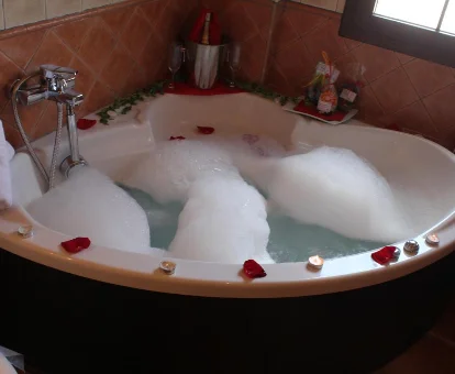 Foto de la bañera de hidromasaje con espuma y pétalos de rosa que se encuentra en ele Hotel Rural Valle del Turrilla - Cazorlatur 
