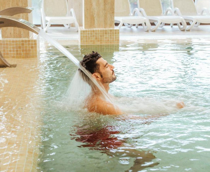 Foto de un hombre en la cascada de la piscina cubierta con tumbonas del spa del hotel Impressive Playa Granada
