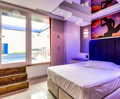 Foto de la habitación con la cama y las luces de toque erótico y donde se ve la piscina privada al fondo detras de los cristales