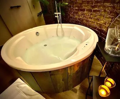 Foto de la bañera de hidromasaje junto a la pared de piedra, llena de agua y con unas velas en el borde