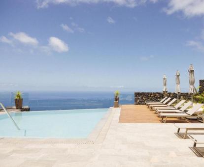 Zona exterior con piscina al aire libre de borde infinito con vistas al mar y solarium con tumbonas.