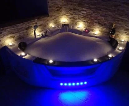Bañera de hidromasaje junto a la pared de piedra con luz azul y velas en el borde además de una botella de cava.