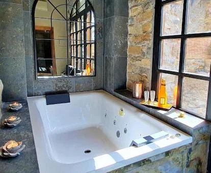 Foto del jacuzzi para dos personas que se encuentra frente a un espejo y al lado de la cristalera que lleva al patio de la suite deluxe con bañera de hidromasaje