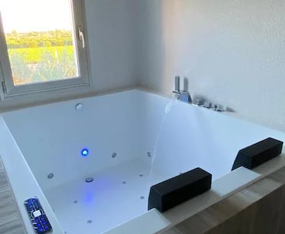 Jacuzzi para dos personas con luz azul de cromoterapia junto a una ventana con vistas al campo en Alicante