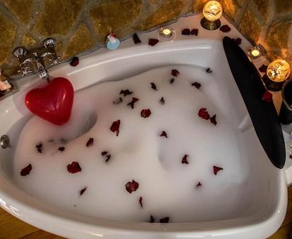 Jacuzzi lleno de espuma, con pétalos de rosa y globos en forma de corazón, y con unas velas en el borde en el baño de la casa de 1 dormitorio en Cazorla Rural