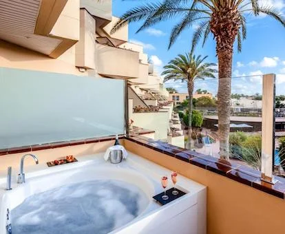 Jacuzzi con unas comas y una botella de cava, y con vistas a la piscina en la terraza de la habitación Deluxe.