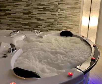 Jacuzzi para dos personas lleno de agua y con burbujas con unas velas de color rojo por el borde