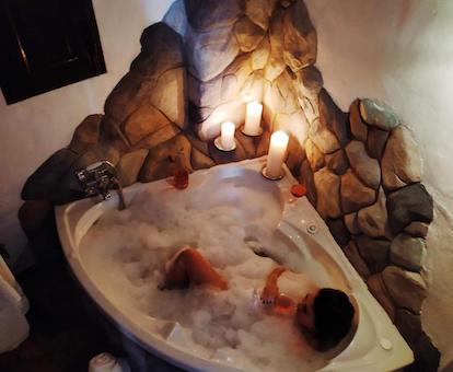 Foto desde arriva de la bañera de hidromasaje de forma triangular, con unas velas encendidas en el borde, y llena de espuma donde se encuentra una chica disfrutando del baño