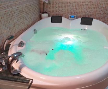 Foto del jacuzzi en el baño con espacio para dos pesonas con su correspondiente respaldo, lleno de agua, con luz verde y con los chorros de hidromasaje funcionando