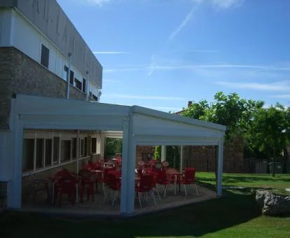 Edificio de este hotel con jardín y mobiliario bajo porche.