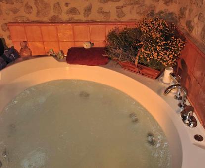 Foto de la bañera de hidromasaje circular llena de agua burbujeante y con jabones y hierbas a un lado.