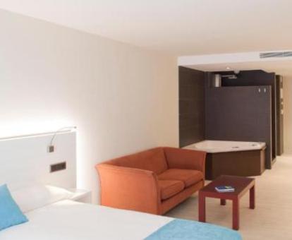 Amplia habitación doble confort con zona de estar y bañera de hidromasaje privada para dos personas cerca de la cama.