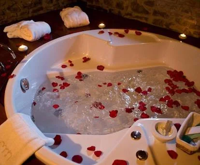 Foto del jacuzzi circular decorado con pétalos de rosas rojas y cremas de tratamientos en uno de los laterales