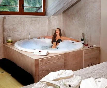 Foto de una mujer relajandose en el jacuzzi de forma circular con una botella de cava junto al border y que se encuentra cerca de la cama