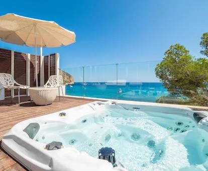 Jacuzzi en la terraza de la Deluxe Double Room con tumbonas, sombrillas y vistas al mar y las montañas