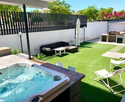 Foto del jacuzzi para cuatro personas en funcionamiento debajo de un toldo en el jardín con mobiliario y la barbacoa al fondo.