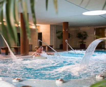 Pareja disfrutando de la piscina con elementos de hidroterapia del centro de bienestar del hotel.