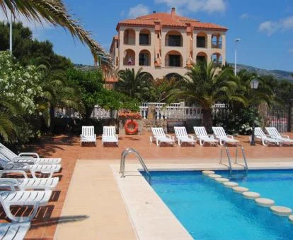 Hotel con encanto con piscina rodeada de tumbonas y de vegetación.