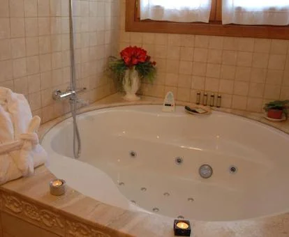 Bañera de hidromasaje circular con unas velas encendidas en el border, junto a la ventana y con unas toallas en el borde en la suite junior con jacuzzi