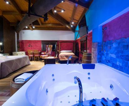 Foto de la bañera de hidromasaje que se encuentra en la Suite en un rincón de la habitación enfrente de la cama en un ambiente romántico y con una iluminación para dar un toque especial al jacuzzi.